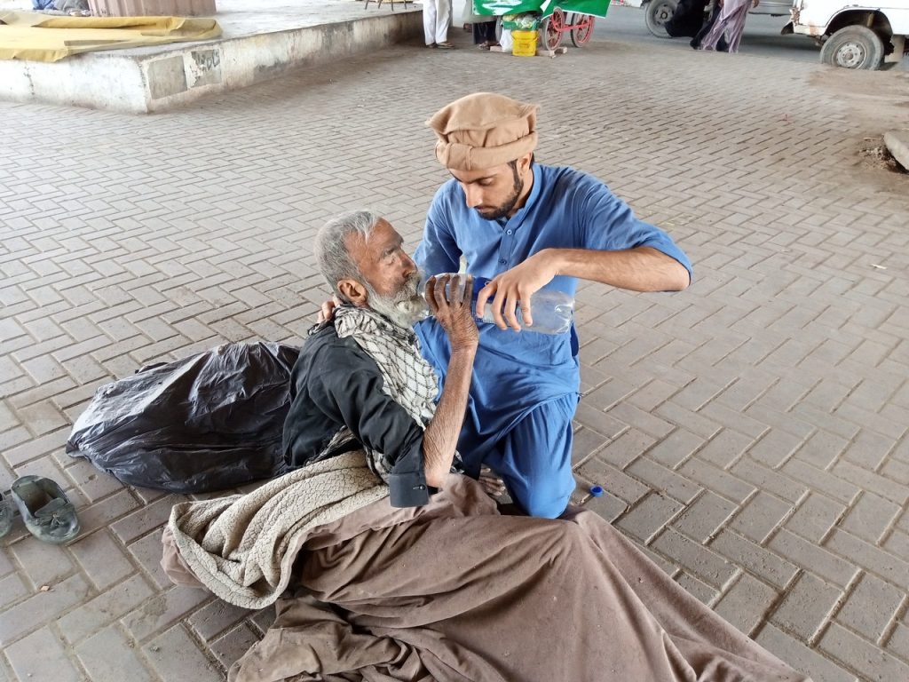 A man in blue clothing gives water to an elderly man
